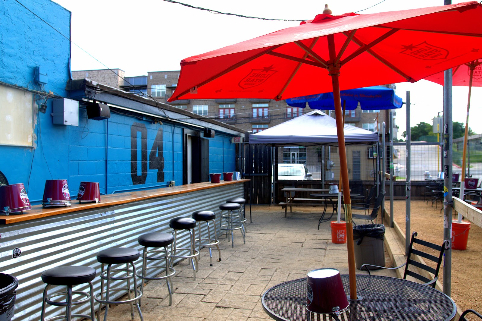 Side patio at The 04 Lounge: blue wall, red umbrellas, and stools along the rail.