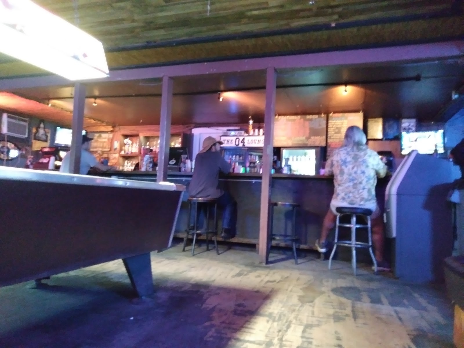 Pool table in the foreground and regulars on stools at the bar.