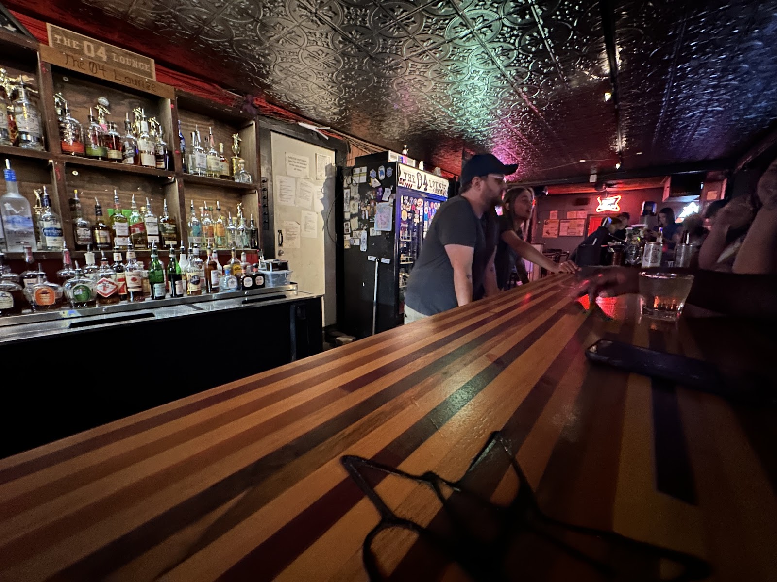 The striped wood bar top, with the liquor shelves and a hand-lettered 04 Lounge sign behind it.